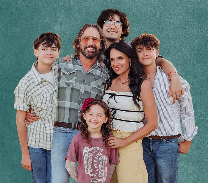 The WallerCo family smiling together in front of a green wall